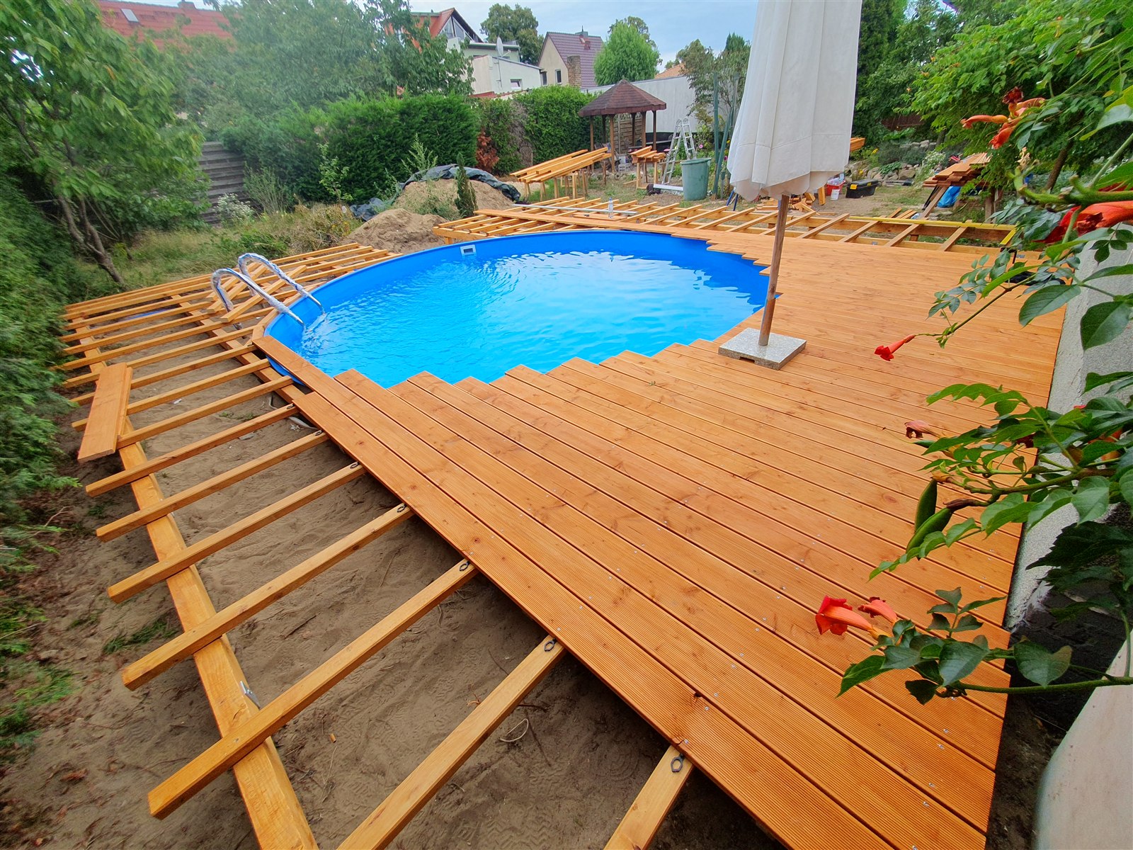 Teilweise montiertes Holzdeck mit offenen Holzträgern neben dem neuen Pool