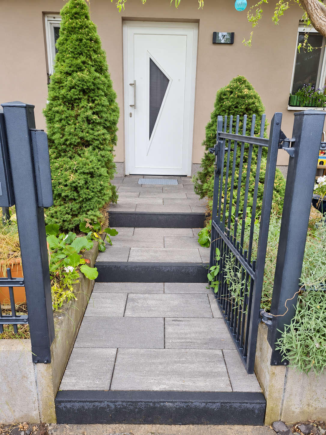 Gestalteter Hauseingang mit grauen Platten, Stufen und eingefasster Bepflanzung