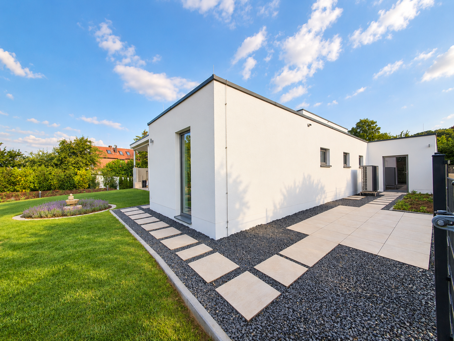 Gartenanlage mit Rasen, Lavendelbeet und hellen Plattenwegen am modernen Wohnhaus