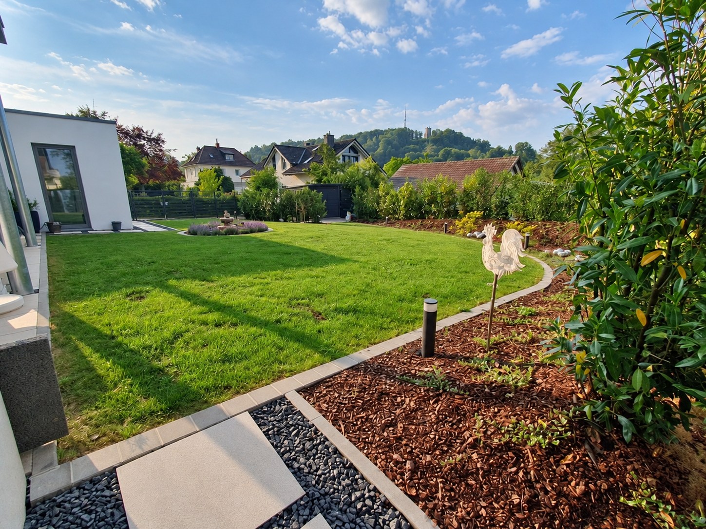Grüne Rasenfläche mit geschwungenen Beeteinfassungen und Gehölzen im Garten