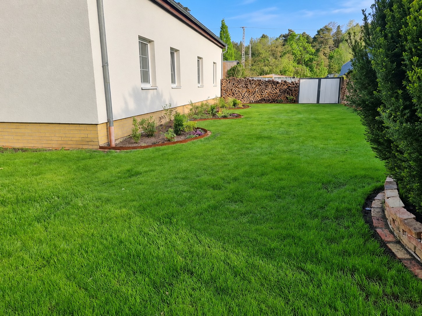 Fertige Rasenfläche mit Pflanzbeeten entlang eines Wohnhauses