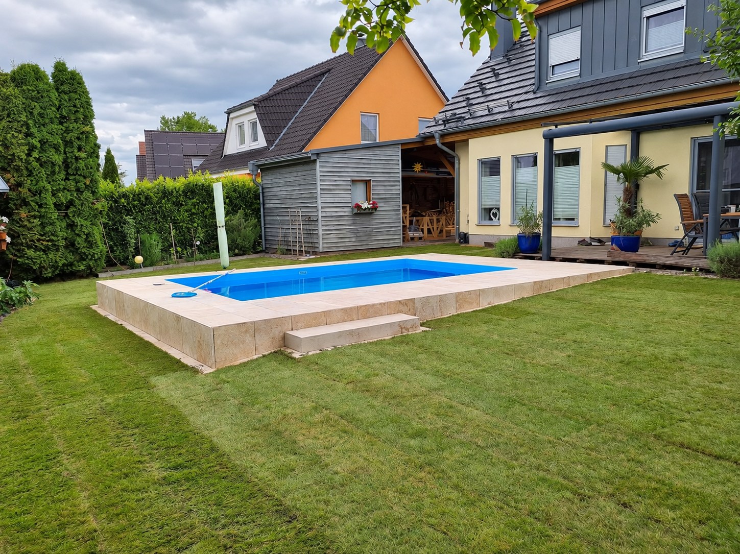 Rechteckiger Gartenpool mit heller Beckenumrandung und Stufe am Wohnhaus