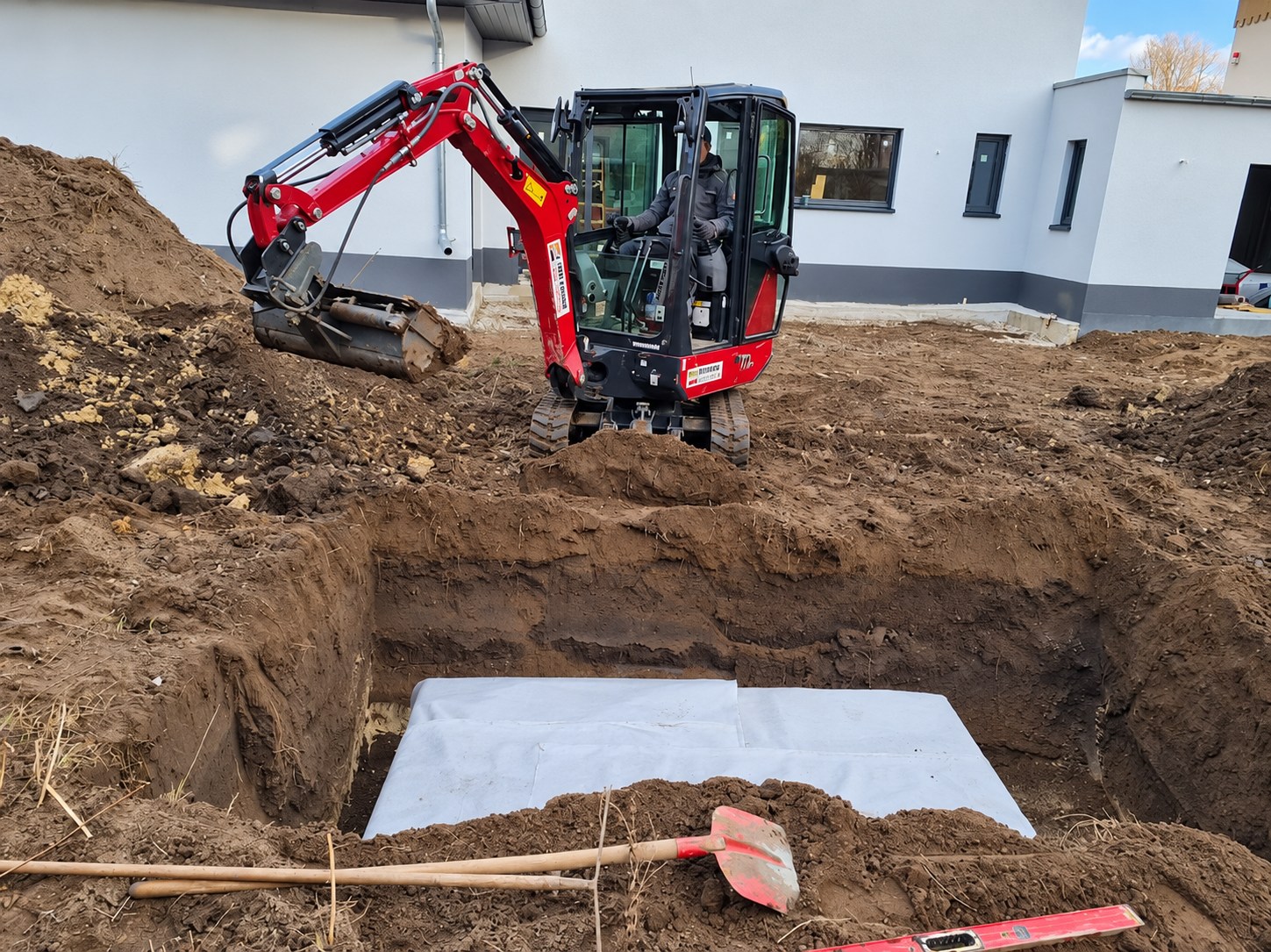 Bagger und vorbereitete Grube mit Vlies für Arbeiten an der Regenentwässerung