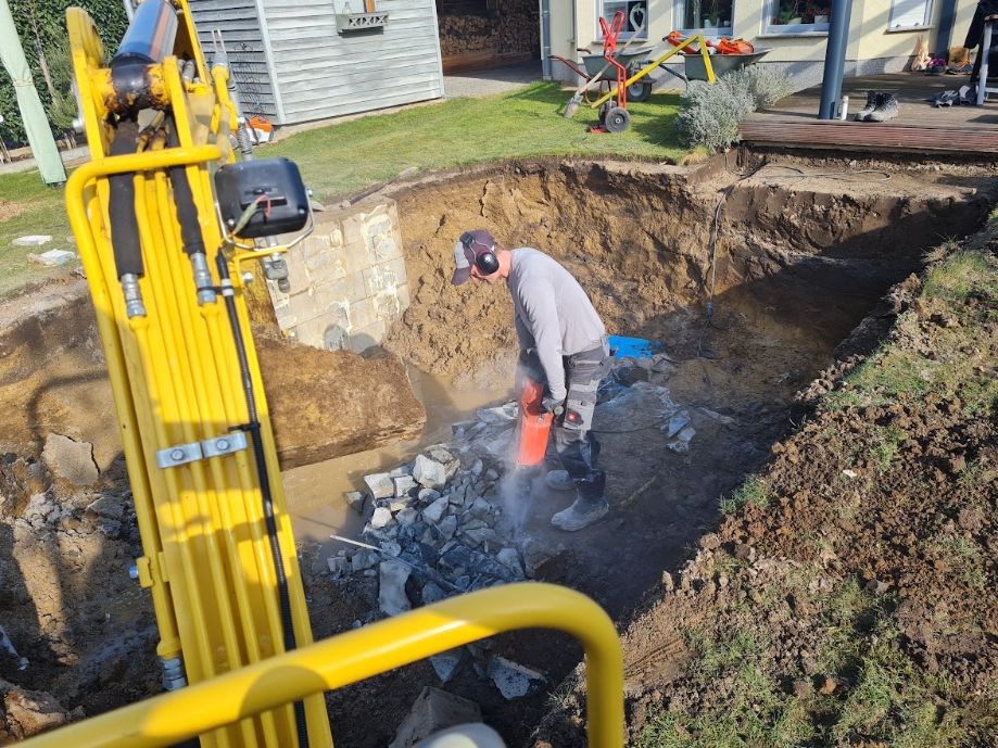 Baustellenarbeiten mit Bagger und Abbruchhammer in einer Gartenbaugrube